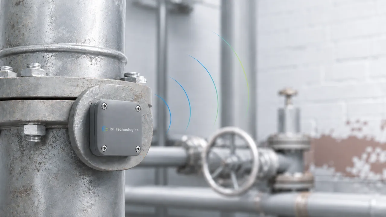 Industrial wireless sensor tag mounted on a steel pipe flange in a plant room, transmitting concentric one-way wavefronts outward with no receiving device present.